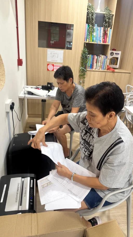 Two seniors sorting paperwork together in a THKMC reading room.
